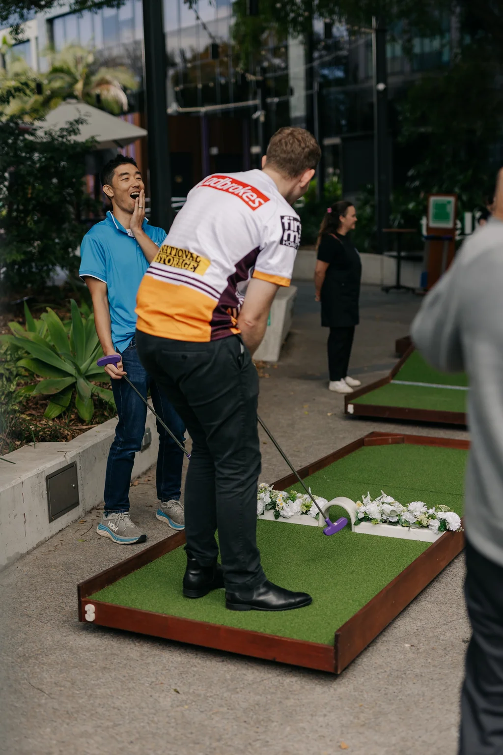Two guests laughing while playing mobile mini-golf outdoors at an event
